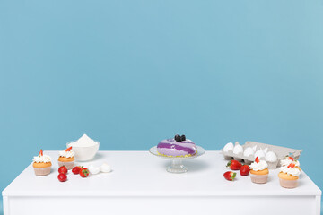 Confectioner baker chef white table with ingredients for cooking cake or cupcake eggs strawberry flour isolated on blue wall background in studio. Mock up copy space food concept. Nobody interior.