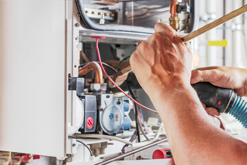 The master sets up a gas boiler, which weighs on the wall. The front dashboard is open. Using a brush and an industrial vacuum cleaner, cleaning from dirt and dirt.