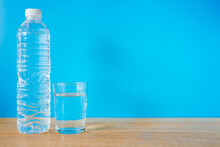 Refreshing Natural Mineral Water In Plastic Bottle With Transparent Glass On Wooden Desk With Blue Background 
