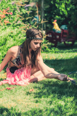 Wall Mural - Portrait of beautiful cute brunette teenager model with makeup, poreo, in summer colorful swimsuit posing on the sea coast. young beautiful young girl in a bathing suit sitting on the grass