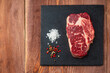 Fresh raw meat with spices and salt and red pepper on black slate, on woden table,