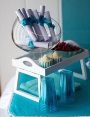 Canvas Print - Vertical  shot of a  wedding rolled paper, cups, and a cupcake placed on a blue table