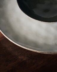 Poster - Closeup shot of a white ceramic plate with a small black bowl on it on a wooden table