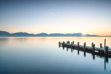 Wall Mural - Wooden pier or jetty at sunrise and sky reflection on water. Versilia Tuscany, Italy