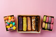 Carton boxes with eclair cakes and cookies on pink surface
