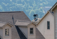 Young Roofing Contractor Replacing The Old Shingles On A Townhouse Roof High Above The Ground