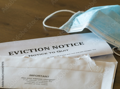 Defaulting renter with facemask receives letter giving notice of eviction from home on wooden table © steheap