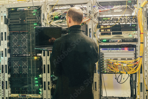 Fotografía An engineer with a laptop is behind the glass in the server room of the data center