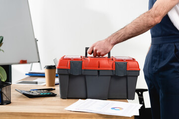 Wall Mural - cropped view of repairman with toolbox on office desk with papers and coffee to go