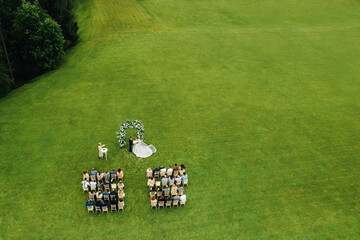 Wall Mural - Top view of the Wedding ceremony in a green field with guests sitting on chairs. Wedding venue on the green lawn.