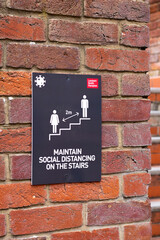 COVID 19 safety information sign for shoppers mounted on brick wall leading to stairs