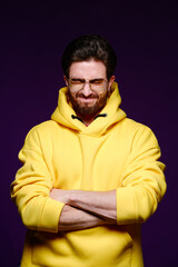 Wall Mural - A young man of 25-30 years in glasses and a yellow sweatshirt emotionally poses on a purple background. 
