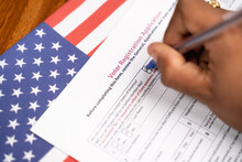 Maski, India - 23, June 2020 : Close Up Of Hands Filling President Voter Registration Application With US Flag As Background For Upcoming Election.