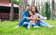 © My Ocean studio - Beautiful happy family while sitting together on the grass and hugging each other, relaxing outdoors on suburban house background.