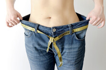 Weight Loss Concept. Woman Shows Her Weight Loss By Wearing An Old Jeans. Healthy Lifestyle. Oversized Jeans.