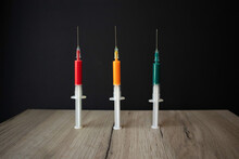 Three Medical Syringes With Colored Liquid Standing Upright On A Wooden Board