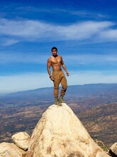 Shirtless Man Standing On Cliff Against Blue Sky