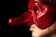 jeune comédien portant un masque de la commedia dell'arte rouge avec un long nez sur fond noir 