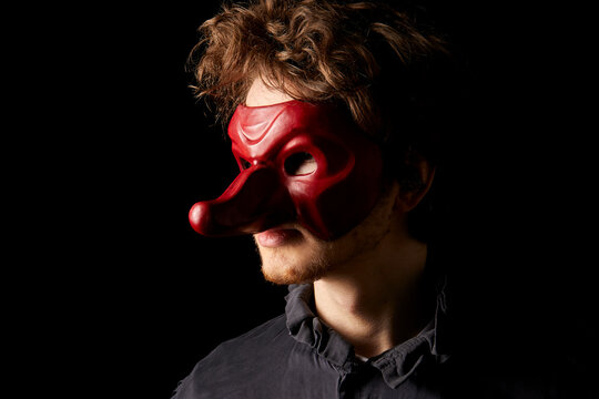 Fototapete -  - jeune comédien portant un masque de la commedia dell'arte rouge avec un long nez sur fond noir 