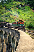 Green And Red Train On The Famous Nine Arches Bridge In Highlands Near Ella, Sri Lanka. Jungle And Tea Plantation All Around.