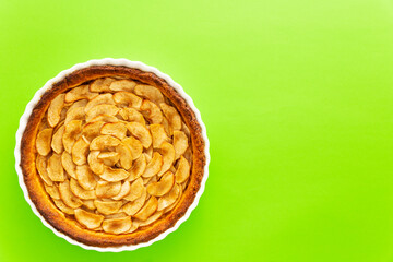 Wall Mural - Homemade baked French apple tart, an open faced apple pie, in a baking white ceramic dish on a green background. Flat lay, top view with copy space.