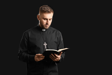 Wall Mural - Young priest with Bible on dark background
