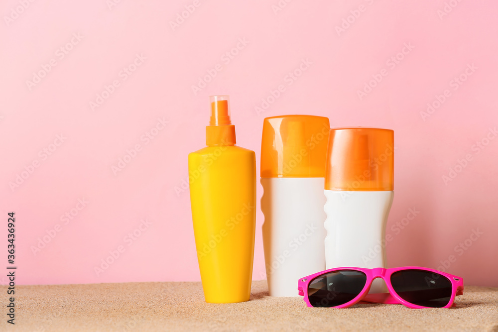 Bottles of sunscreen with sunglasses on color background