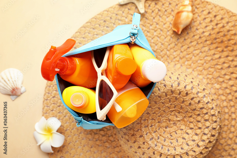 Bag with sunscreen cream, hat and sunglasses on color background