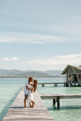 Wall Mural - Couple in love stand on wooden pier with wooden overwater bungalow on background and kiss each other. Vacation by the sea