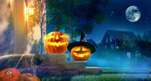 Jack O’ Lanterns Glowing At Moonlight In Night. Spooky Pumpkin In Witch Hat. Halloween Design With Copy Space. Halloween Pumpkins And Decorations Outside On Porch Of House.