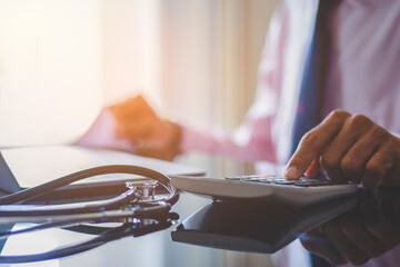 Wall Mural - Smart doctor hand using calculator for account about medical costs with stethoscope and computer notebook on the desk at modern office,clinic or hospital. Healthcare costs and fees conceptual.