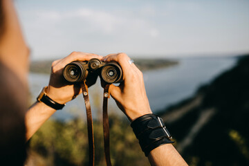 Close-up of a man holding binoculars in mountains.