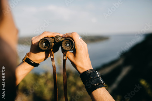 Close-up of a man holding binoculars in mountains.