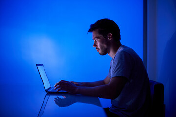 Hacker tries to break security system to steal important company information, working at laptop in blue neon light