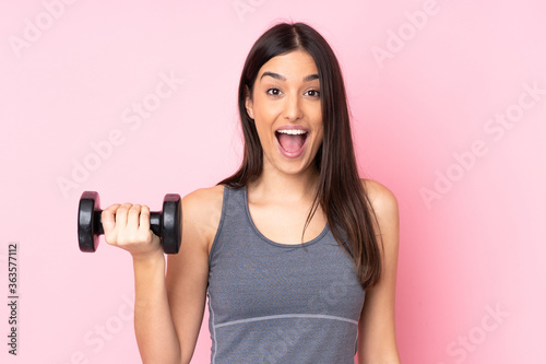 Fotografía Young woman making weightlifting isolated on pink background with surprise and s