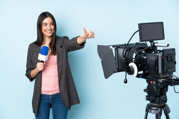 Wall Mural - Reporter woman holding a microphone and reporting news isolated on blue background giving a thumbs up gesture