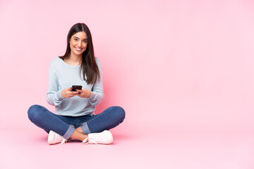 Wall Mural - Young caucasian woman isolated on pink background sending a message with the mobile