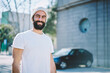 © BullRun - Half length portrait of handsome hipster guy in white t-shirt with advertising area for brand name enjoying free time outdoors, bearded smiling male hispanic model standing on urban setting background