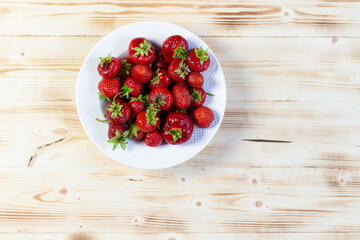 Wall Mural - Flat lay on White plate with ripe red fresh strawberry on wooden table