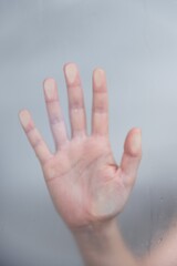 Wall Mural - Vertical shot of a hand behind on a moist glass