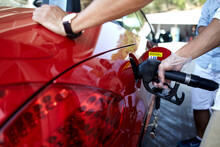 Cropped Shot View Of A Young Man Pumping Gasoline Fuel In His Luxury Red Car Cabriolet At Gas Station While Stopping During Road Trip With Friends, Transportation And Expenses Concept