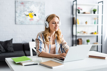 Selective focus of pretty woman working with laptop and headphones