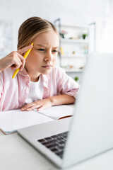 Wall Mural - Selective focus of focused kid holding pen and looking at laptop