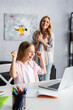 © LIGHTFIELD STUDIOS - Selective focus of smiling child showing yeah gesture during online education near positive mother at home