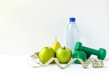 Green apples, dumbbells, measuring tape and a water bottle on a white background. The concept of a healthy lifestyle, fitness and proper nutrition.