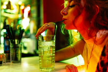 Side View Of A Woman Long Hair Drinking From A Straw A Glass Of Soda Or Alcohol In A Night Club Bar