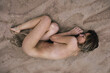 © Evgenij Yulkin/Stocksy - Young naked woman laying on the sand in an embryo position