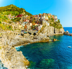 Wall Mural - A view across the rocky coastline towards the village of Manarola, Cinque Terre, Italy in summertime