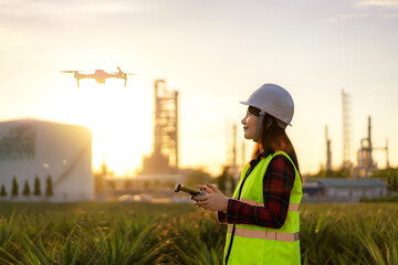 Wall Mural - Asian woman engineer operate flying drone over oil refinery plant during sunrise building site survey in civil engineering project.