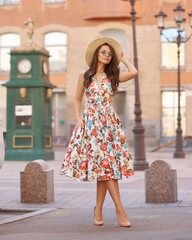Young woman in colorful dress walking city street on a sunny summer day. Full length portrait. Elegant lady with long wavy hair. Girl in sunglasses